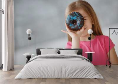 Adorable little girl,a brunette with long straight hair and brown eyes,dressed in a pink summer dress ,holding a fresh donut with chocolate glaze,posing on grey background Wall mural