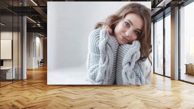 Cute young girl in a gray knitted sweater. Beautiful woman is relaxing in a white bedroom. Beautiful women in winter clothes are waking up in the morning. Woman wearing a sweater in a white bedroom. Wall mural