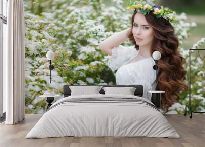 Portrait of a beautiful woman in a wreath of flowers,long curly red hair,gray eyes,a beautiful smile,dressed in a white summer dress posing near spring Bush of a blossoming white flowers Wall mural