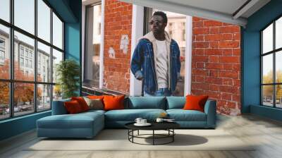 fashion african man wearing jeans jacket poses on city street, brick wall background Wall mural