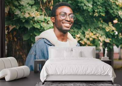 Portrait of happy smiling african man looking away wearing an eyeglasses in autumn city park Wall mural