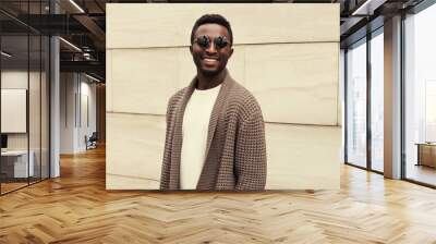 Portrait of stylish smiling young african man wearing brown knitted cardigan on city street background Wall mural