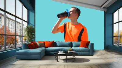 Portrait of tired runner man drinking from bottle the water or protein shake, male sportsman resting after hard training isolated on blue background Wall mural