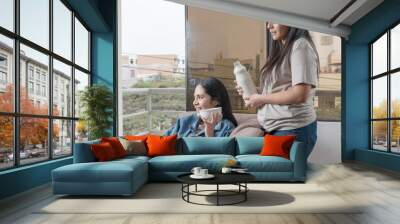 Woman serving handmade almond and coconut milk to a woman sitting on a sofa at home Wall mural