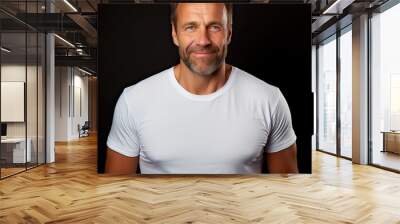 Middle aged good looking man in white t shirt posing in front of a black background with copy space Wall mural