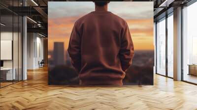 Back view of a man wearing sweatshirt standing on a high place with sky and city blurred background Wall mural