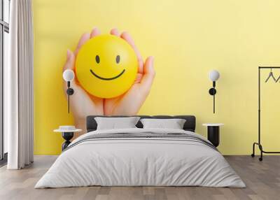 Woman hands holding happy smiling face emoji on isolated yellow background with space for copy Wall mural