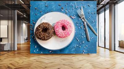 Strawberry and chocolate donuts were designed on plates with decorative candies on a blue surface. Wall mural