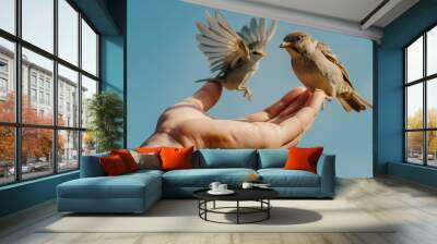 A hand feeds two birds, with one bird flying and the other perched on the fingers, capturing a delicate moment of connection with nature and a sense of trust. Wall mural