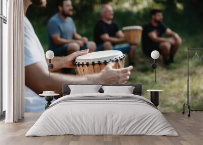 A person playing a hand drum in an outdoor setting, with a group of other drummers in the background, depicting a musical gathering, rhythm, and community spirit. Wall mural