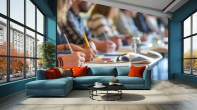 A sharp focus on the hands and pens of students taking notes during a lecture in a classroom Wall mural