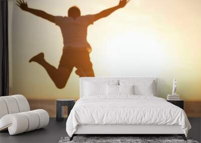 A silhouette of a person leaping joyfully against a stunning sunset, symbolizing freedom, exhilaration, and the beauty of life, showcasing an energetic and carefree moment. Wall mural