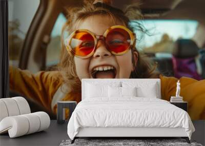 A young girl bursts into laughter, wearing oversized sunglasses, while sitting in a car, exuding pure joy and the carefree spirit of childhood, with excitement palpable. Wall mural