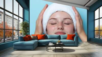 Two hands gently hold a warm, white towel, presenting a calming and inviting scene suggestive of spa treatment or relaxation against a clean, soothing blue background. Wall mural