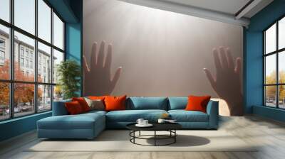 Two hands reach upwards towards a radiant light source in an otherwise dark space, symbolizing hope, aspiration, and the pursuit of enlightenment and inspiration. Wall mural