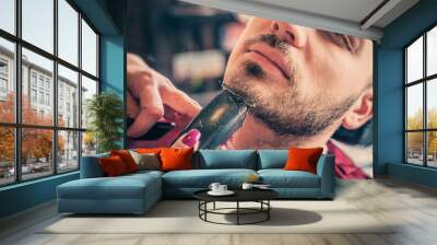 Female barber shaving a client's beard with trimmer in a barber shop. Close-up Wall mural