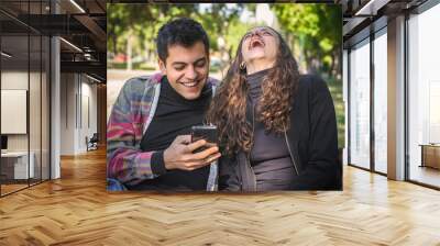 Smiling couple looks photos and reads messages on mobile phone Wall mural