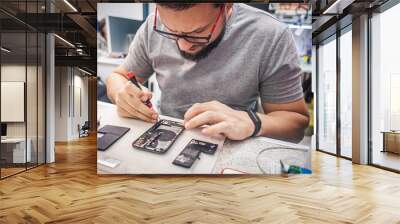 Workplace top view, close-up. Repairman disassembles smartphone with screwdriver in an electronics repair shop. Wall mural