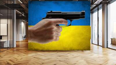 Hand holding a gun on ukraine flag background on war conflict. Wall mural