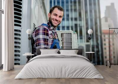 HVAC Technician with Air Conditioning Unit. Friendly HVAC technician in plaid shirt and overalls servicing an air conditioning unit with urban buildings in the background. Wall mural