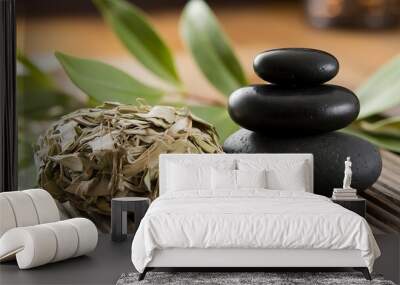 Three black stones stacked on a wooden surface with dried leaves and a green plant in the background. Wall mural