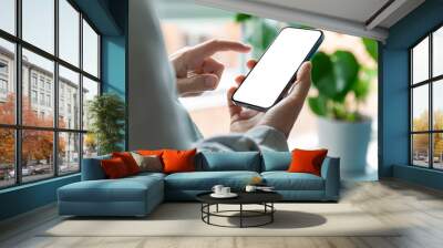 A man is using a smartphone with a blank, frameless  screen in a contemporary home or office interior. Bright light with plants in the background Wall mural