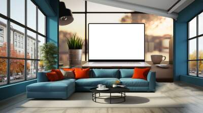 Laptop with blank screen on table in livingroom during golden sunset or sunrise - home office background Wall mural