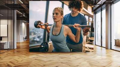 Young beautiful woman doing exercise at the gym with her personal trainer. Wall mural