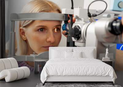 close up in an ophthalmology clinic young doctor diagnoses the eyes of a young girl with a magnifying lens Wall mural