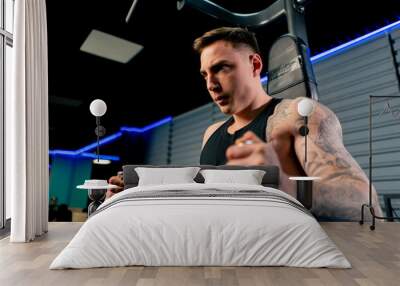 close up in the gym a young handsome guy with tattoos pumps up his abs on the horizontal bar Wall mural