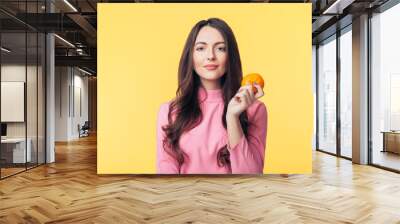 Beautiful young woman holding orange in hand isolated on yellow background Wall mural