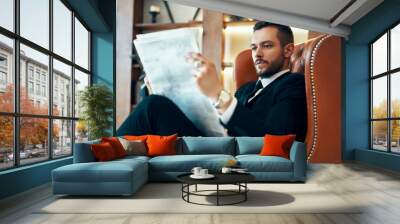 Confident young businessman reading newspaper and latest news while sitting in armchair Wall mural