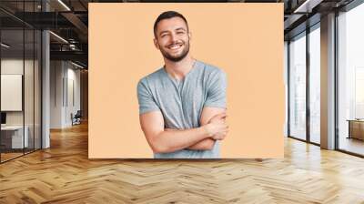 Happy smiling handsome man with crossed arms looking to camera over beige background Wall mural