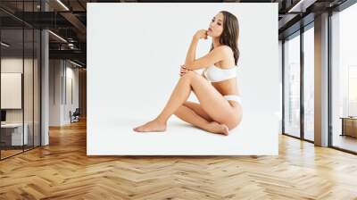 Perfect young woman with sporty body in underwear sitting on floor posing on white studio background Wall mural