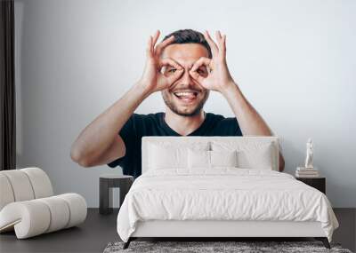 Young creative man holding fingers near eyes like glasses Wall mural