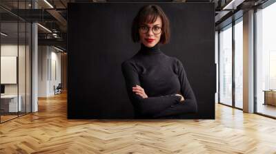 Close-up studio shot of young woman wearing eyewear and red lipstick while standing at dark background Wall mural