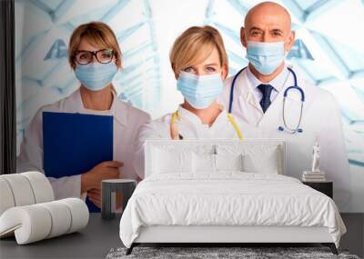 Female medical worker wearing face mask and giving thumbs up while standing together with her colleagues Wall mural