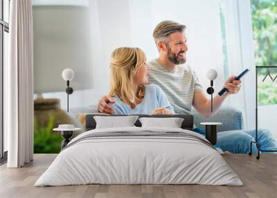 Happy woman and man sitting on the sofa at home and watching tv together Wall mural