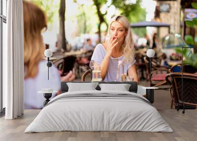 Happy young woman smoking cigarette and sitting outdoors at the cafe terrace Wall mural