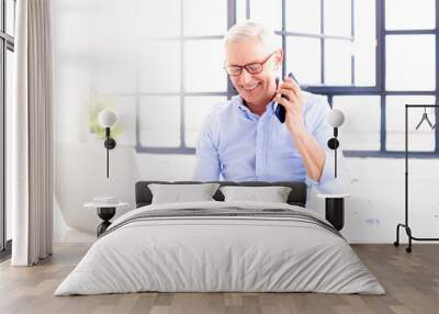 Senior businessman making a call while working on his notebook at home Wall mural