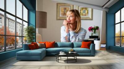 Thinking middle aged woman sitting at desk while working from home Wall mural