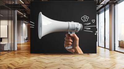 A hand holds a white megaphone against a black background, with drawings of a flower, a heart, and a musical note coming out of the megaphone Wall mural