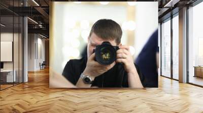 A male photographer holds camera in his hand concept. The self-portrait is reflected in the mirror. Wall mural