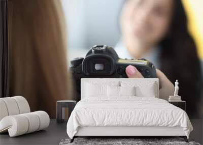 Black camera in hands of woman photographer with woman model on background in photo studio. Home photo session of friends tfc concept. Wall mural