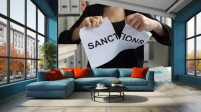 Businesswoman tears up sheet of paper with sanctions inscription Wall mural