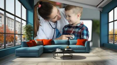 Close-up of smiling kid at doctors appointment. Professional pediatrician listening to heartbeat and checking child lugs. Planned checkup. Medicine and healthcare concept Wall mural