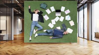 Coworkers lay tired on grass, exhausted employees surrounded with papers, business documentation Wall mural