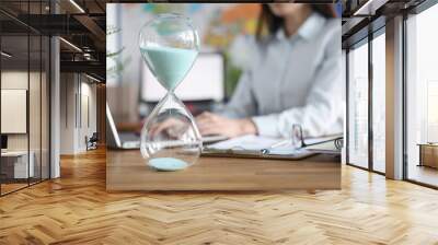 Glass hourglass standing against background of woman working at laptop closeup Wall mural