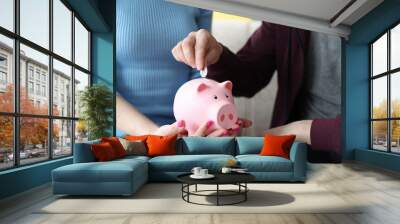 Man putting coin into pink piggy bank in hands of his wife closeup Wall mural