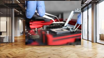 Manual assembly and repair mechanical device. Hands in blue gloves hold tongs. Technician collects metal parts and mounts them on device lying on table. Small parts are attached with tweezers. Wall mural